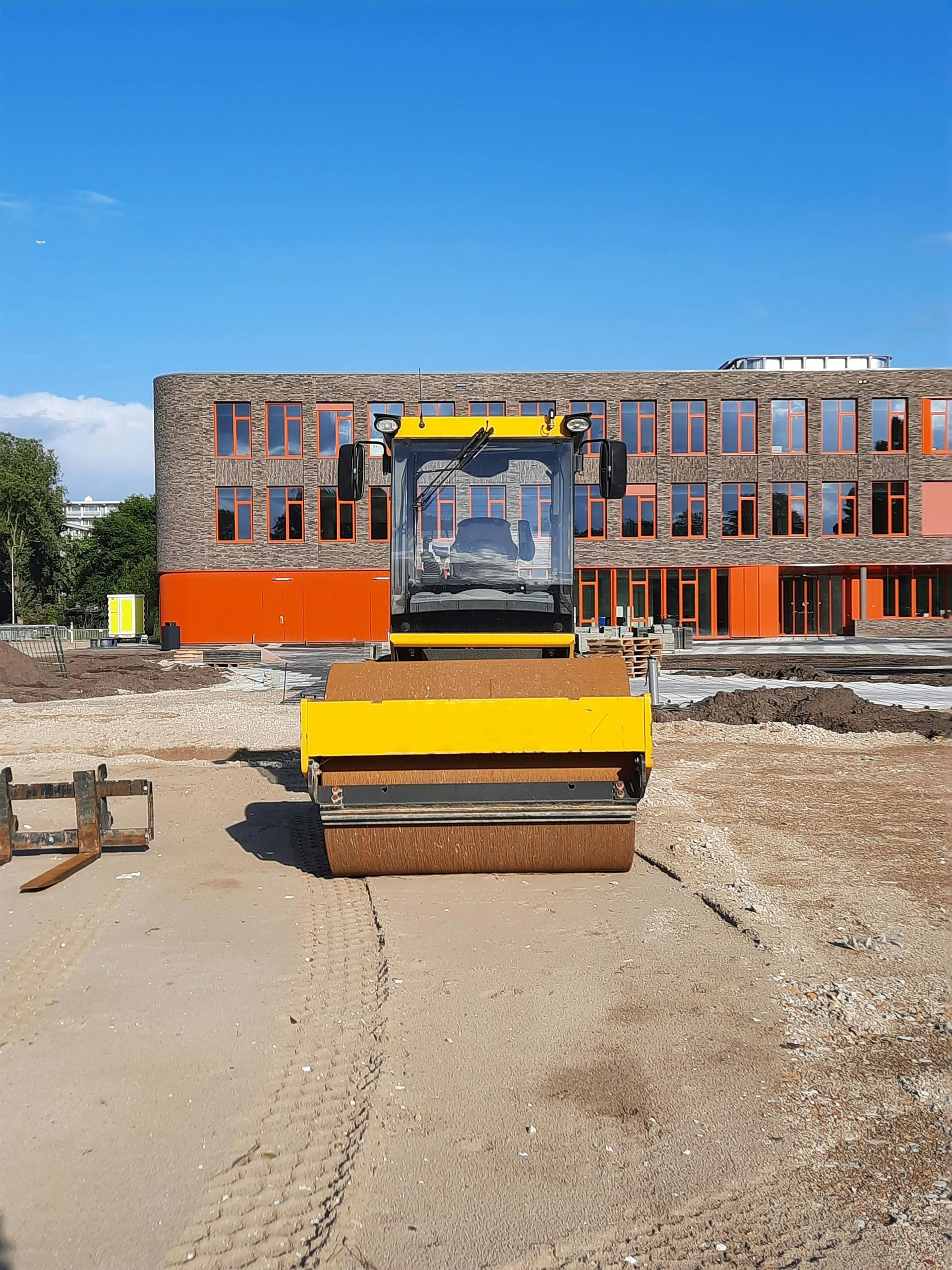 Yellow excavator at a construction site in front of a brick building under a blue sky