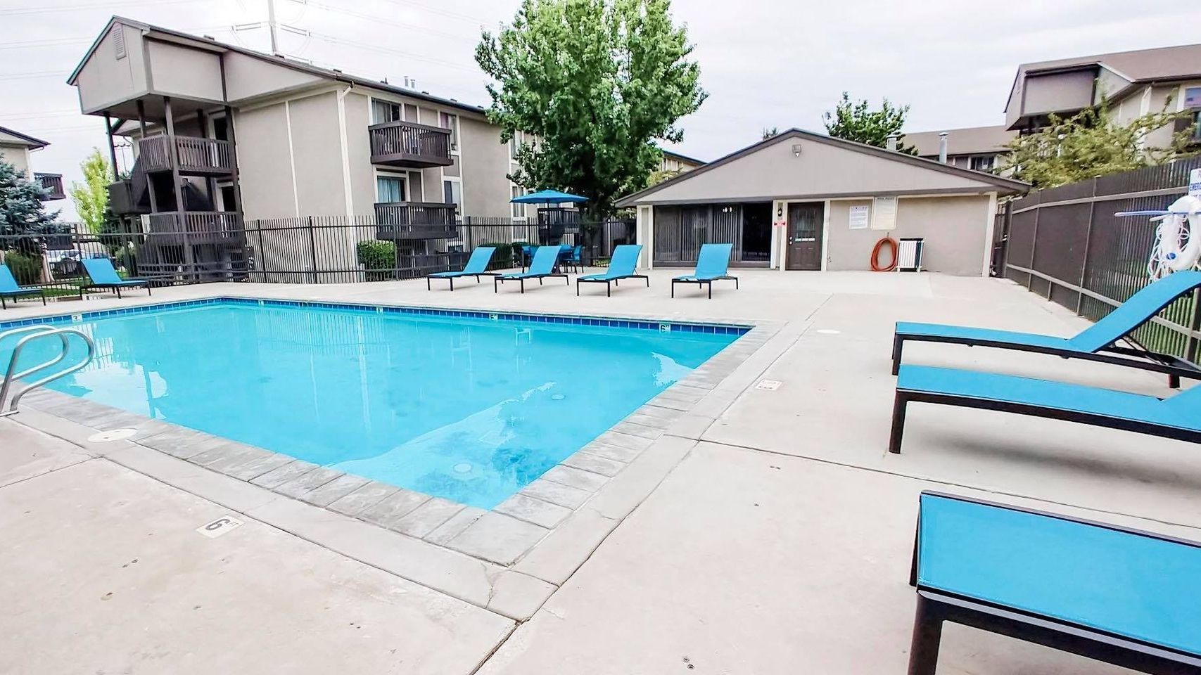 a large swimming pool with blue chairs and a building in the background .