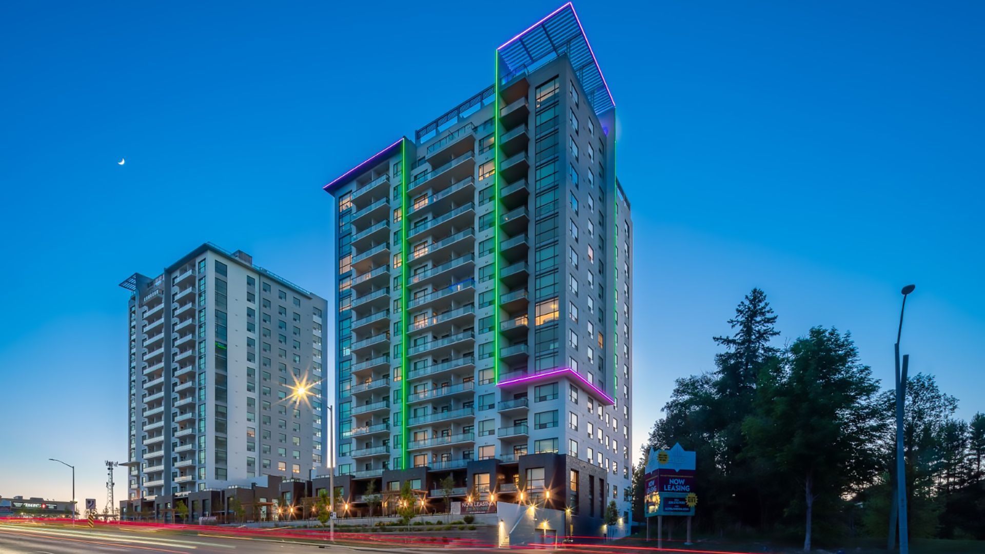 Two tall apartment buildings at dusk, with colorful lights on their facades.