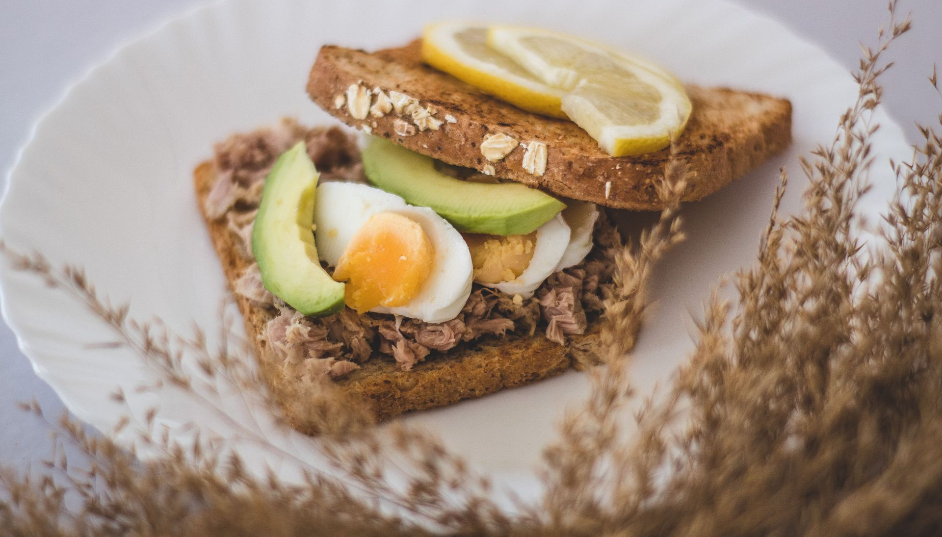 Avocado en zachtgekookt ei op geroosterd brood, gegarneerd met citroen, op een rustieke ondergrond.