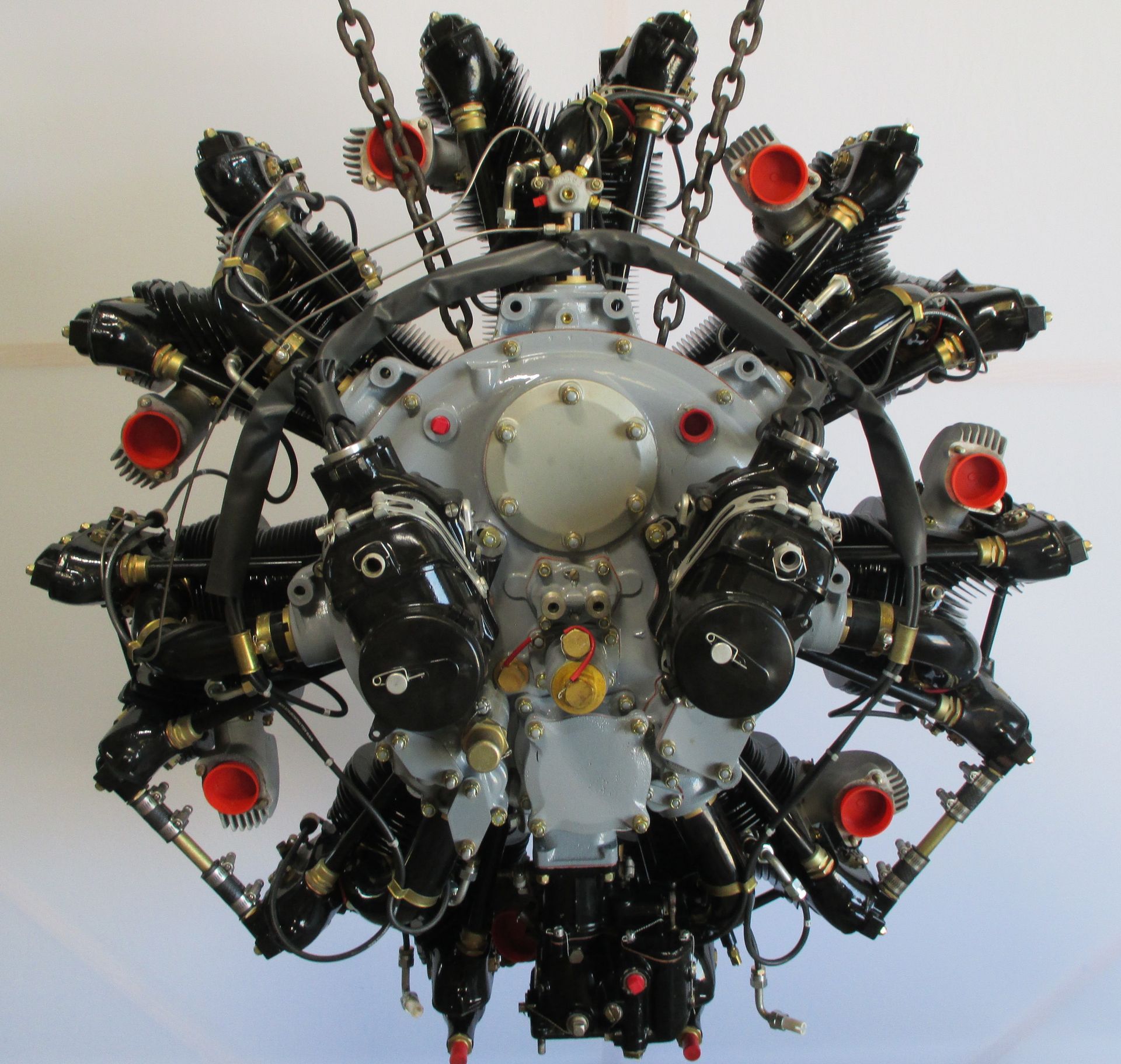 An aviation radial engine, painted gray and black, suspended by chains.