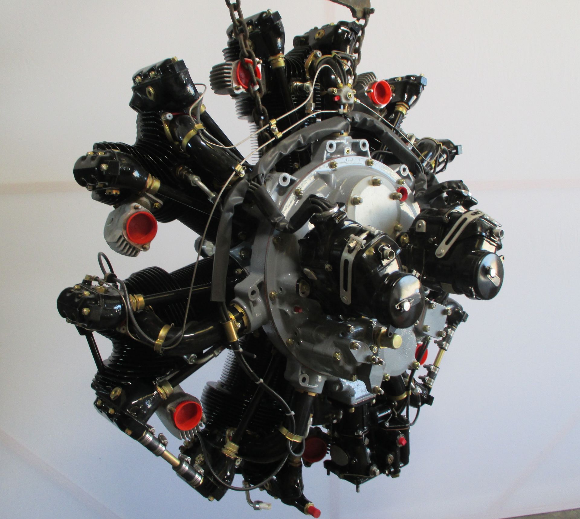 Radial aircraft engine, black with red and silver accents, suspended from chains.