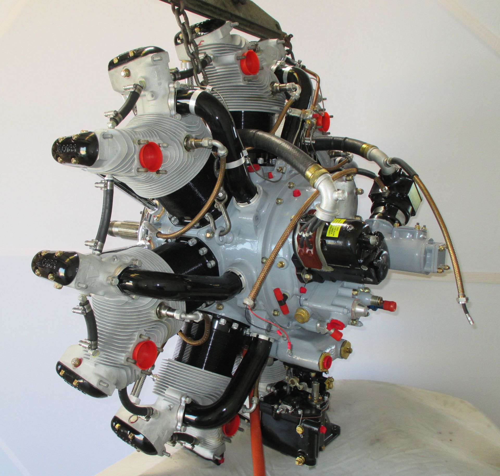 Radial aircraft engine with grey cylinders, red caps, and black tubes.