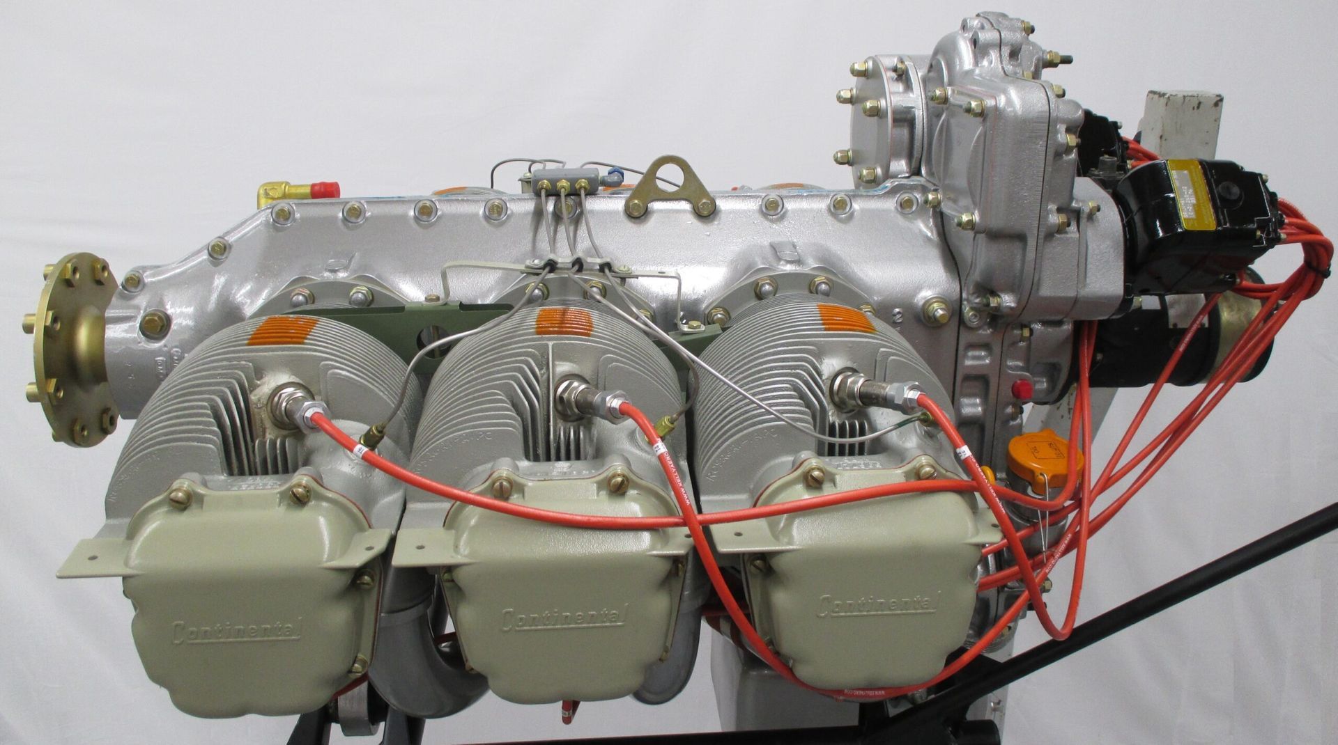 A silver aircraft engine with three cylinders and orange wiring.