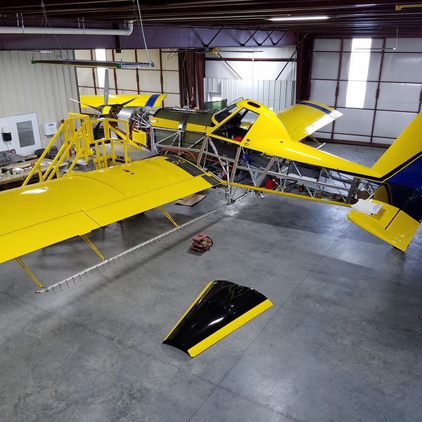 Yellow crop duster plane under repair in a large workshop.