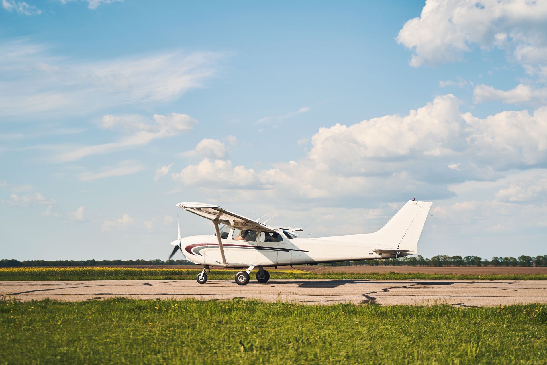 White single-engine airplane on a runway, under a blue sky with fluffy clouds.