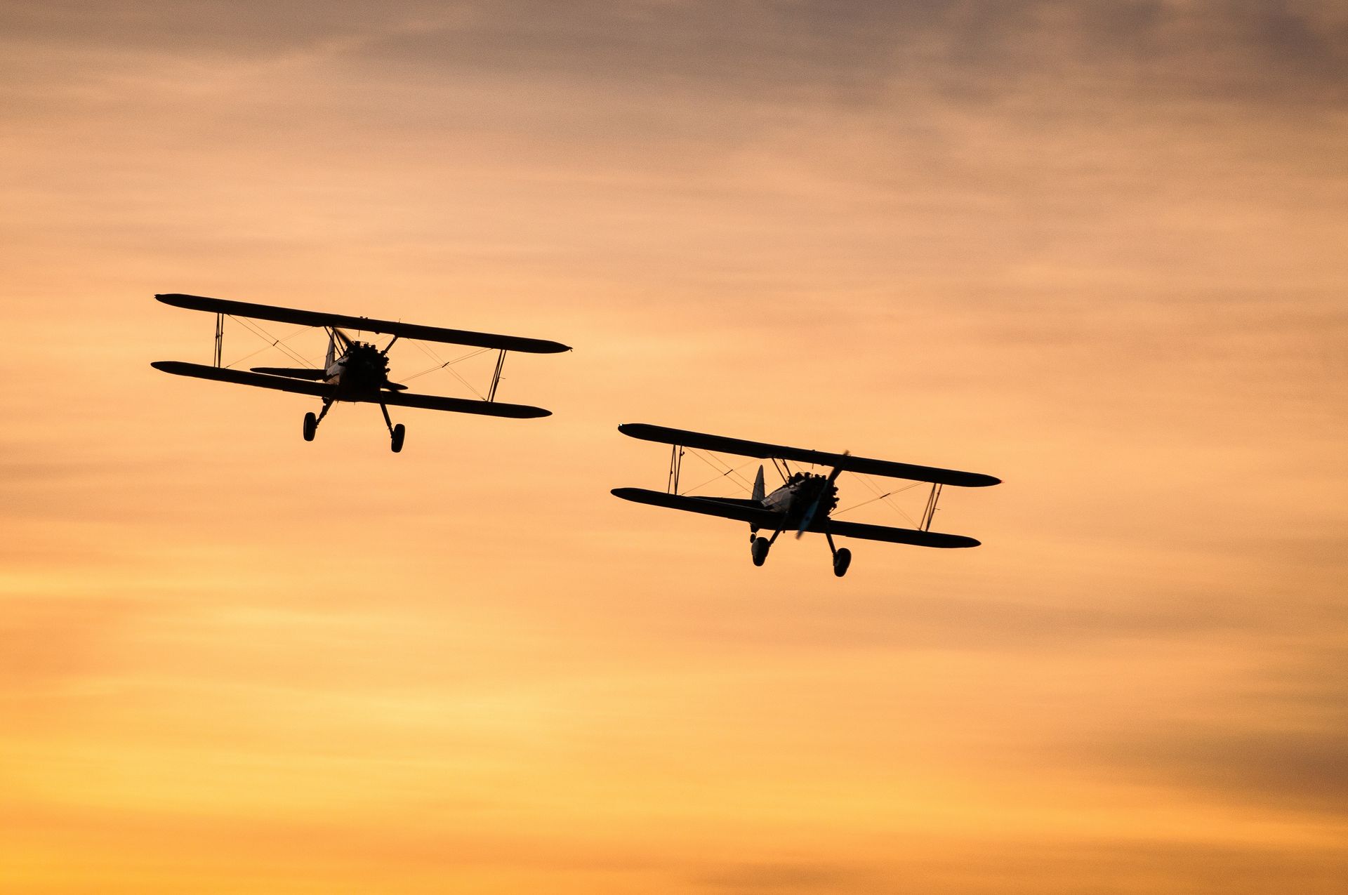 Two biplanes silhouetted against an orange sunset sky.
