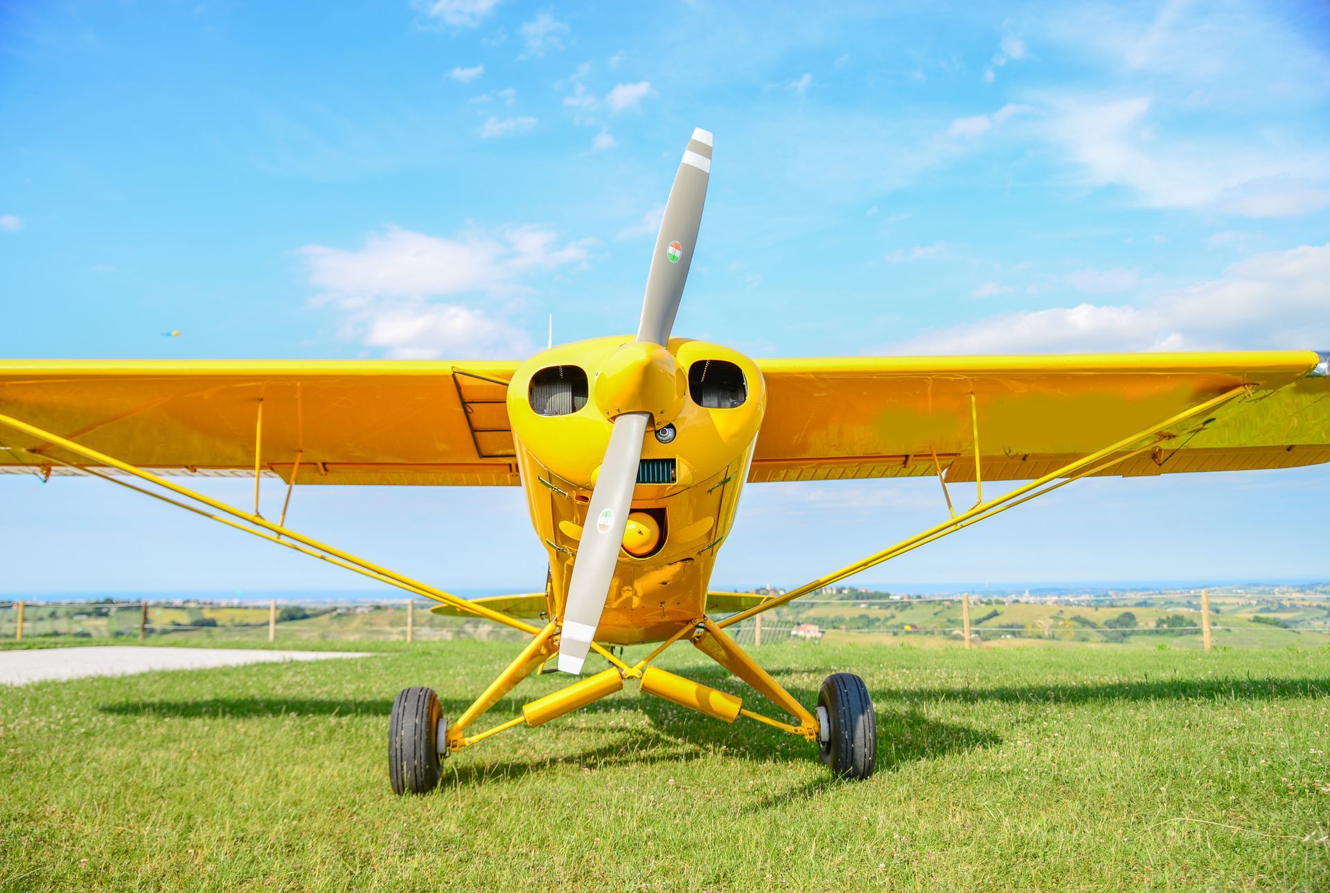 Yellow propeller airplane on grass field, blue sky in background.