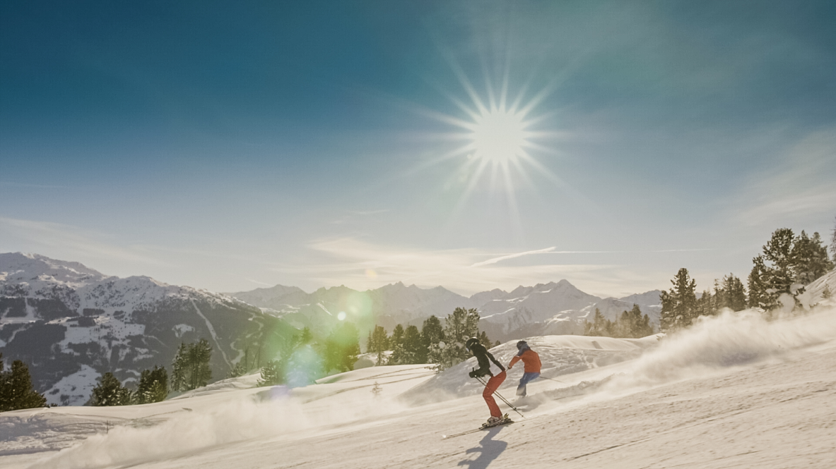 Dwie osoby jeżdżą na snowboardzie po pokrytym śniegiem stoku w słoneczny dzień.