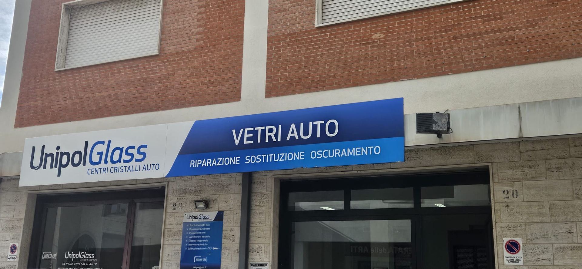 Vetrina con insegne UnipolGlass e VETRI AUTO su un edificio in mattoni