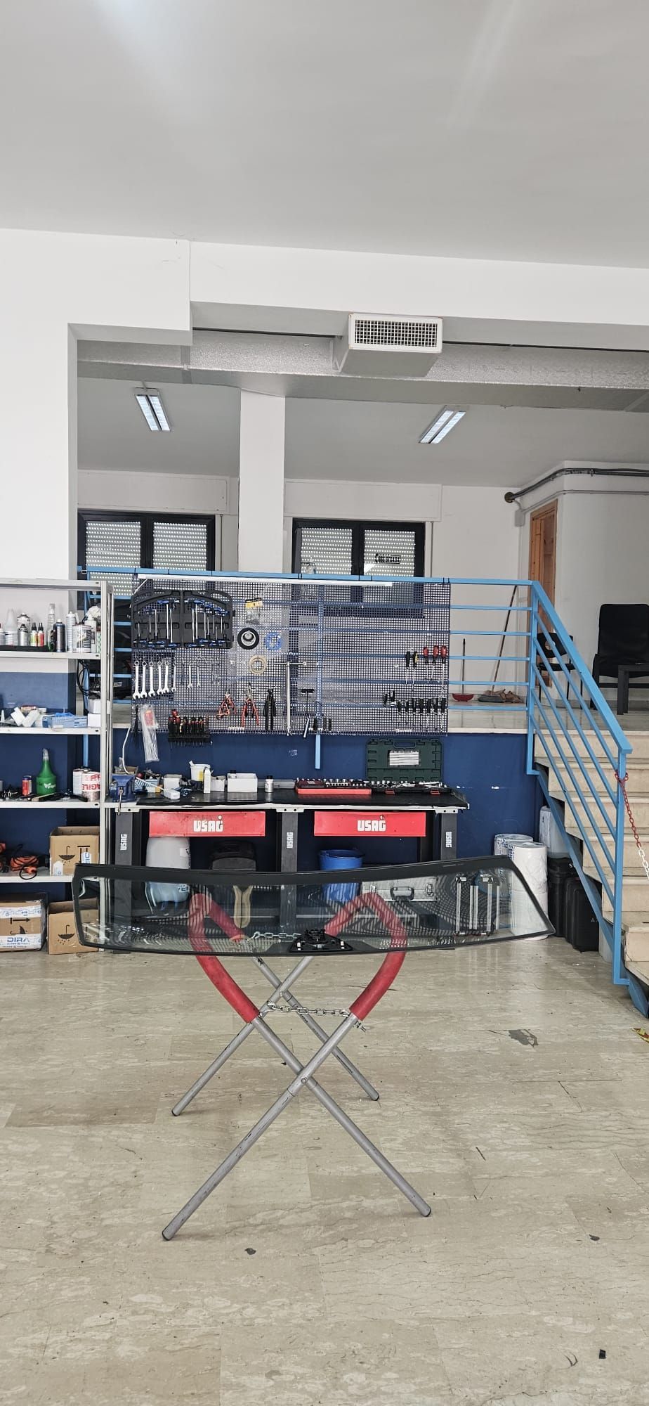 Interno di un'officina con tavolo pieghevole, scaffali, attrezzi e ringhiera blu per le scale.