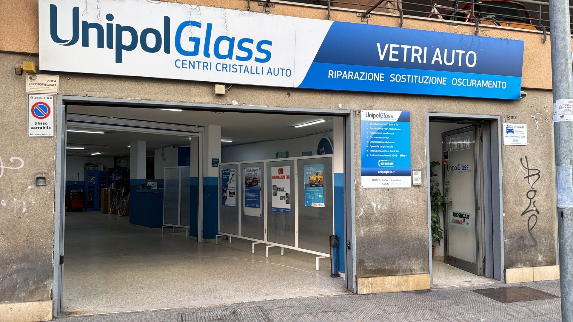 Vetrina del negozio di riparazione vetri auto UnipolGlass con insegna blu e ingresso aperto.