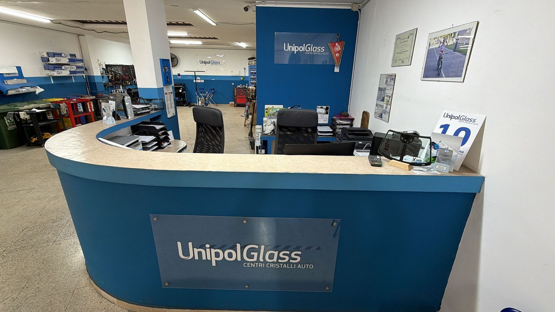 Banco reception dello showroom UnipolGlass con pareti blu, monitor e un dipendente seduto