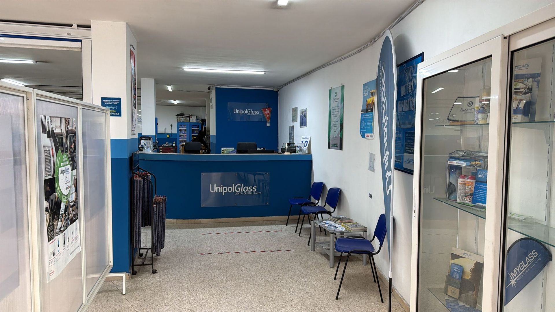 Bancone della reception blu in uno stretto corridoio della clinica, con sedie e vetrine lungo le pareti.