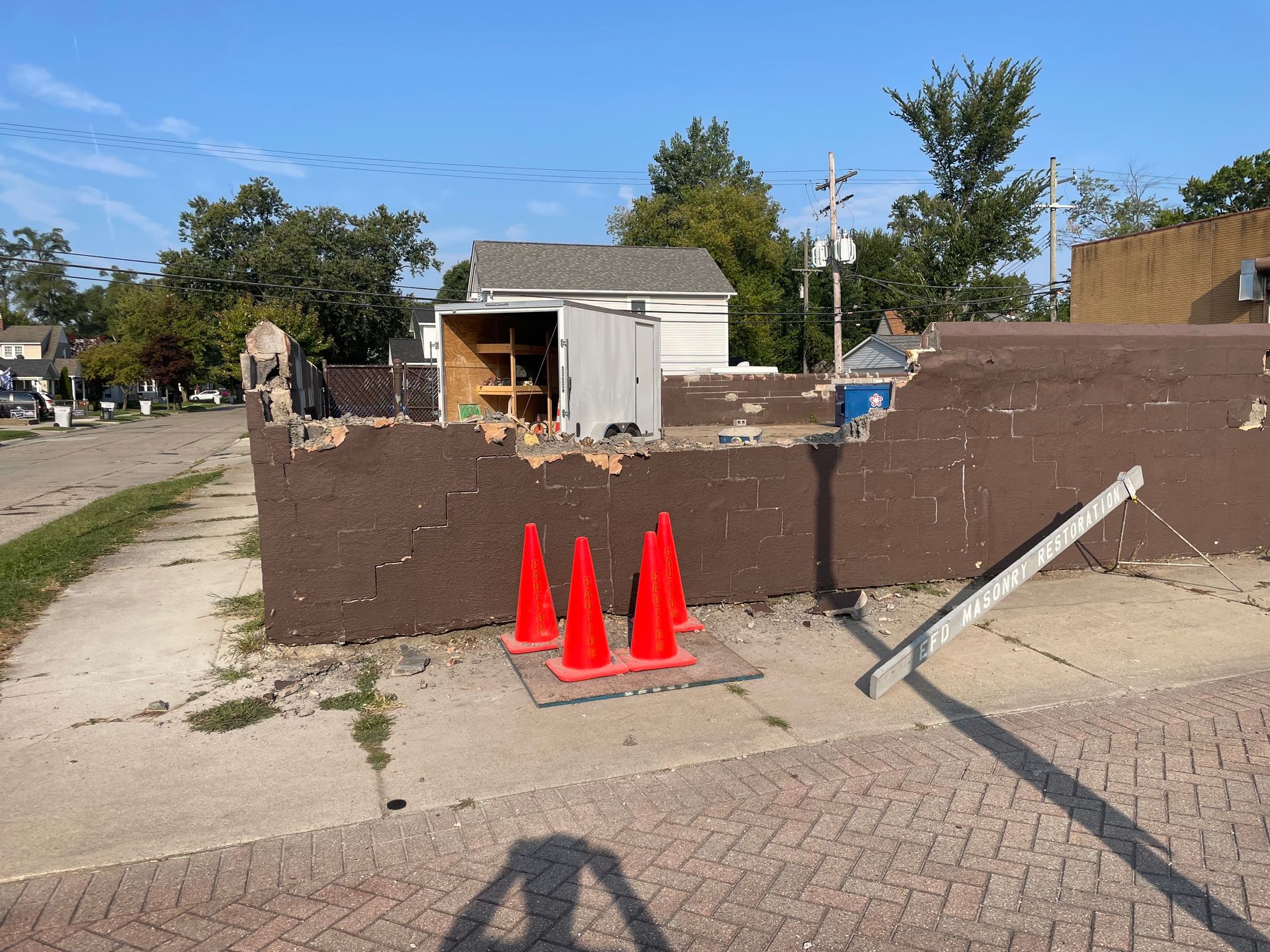 Construction site with brown barrier wall, orange cones, and a small shed under clear sky