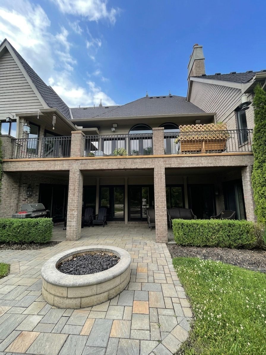 Stone patio with fire pit facing a large rustic house with balcony and blue sky