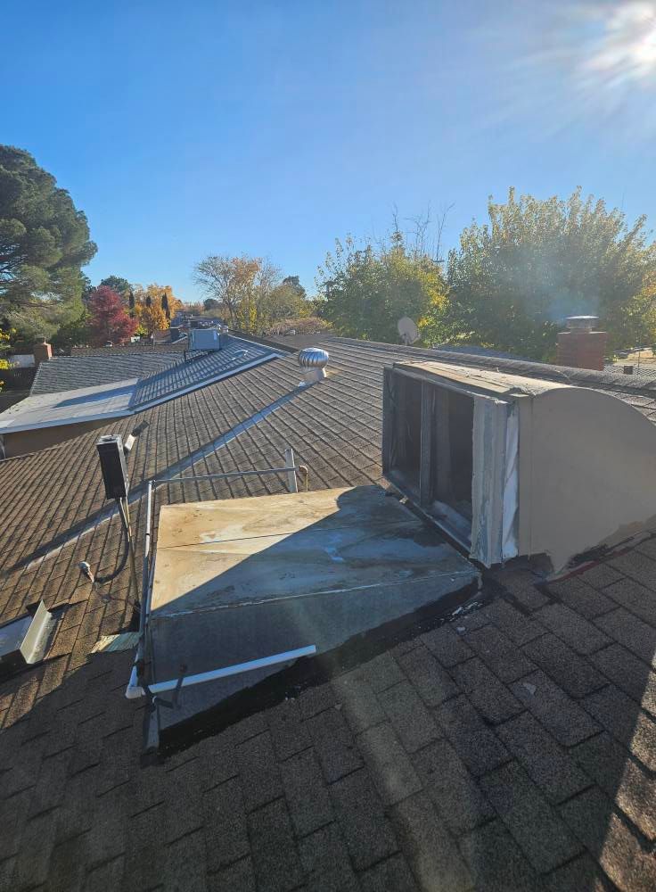 A rooftop view showing a HVAC unit, a satellite dish, and dark asphalt shingles under a clear blue sky.