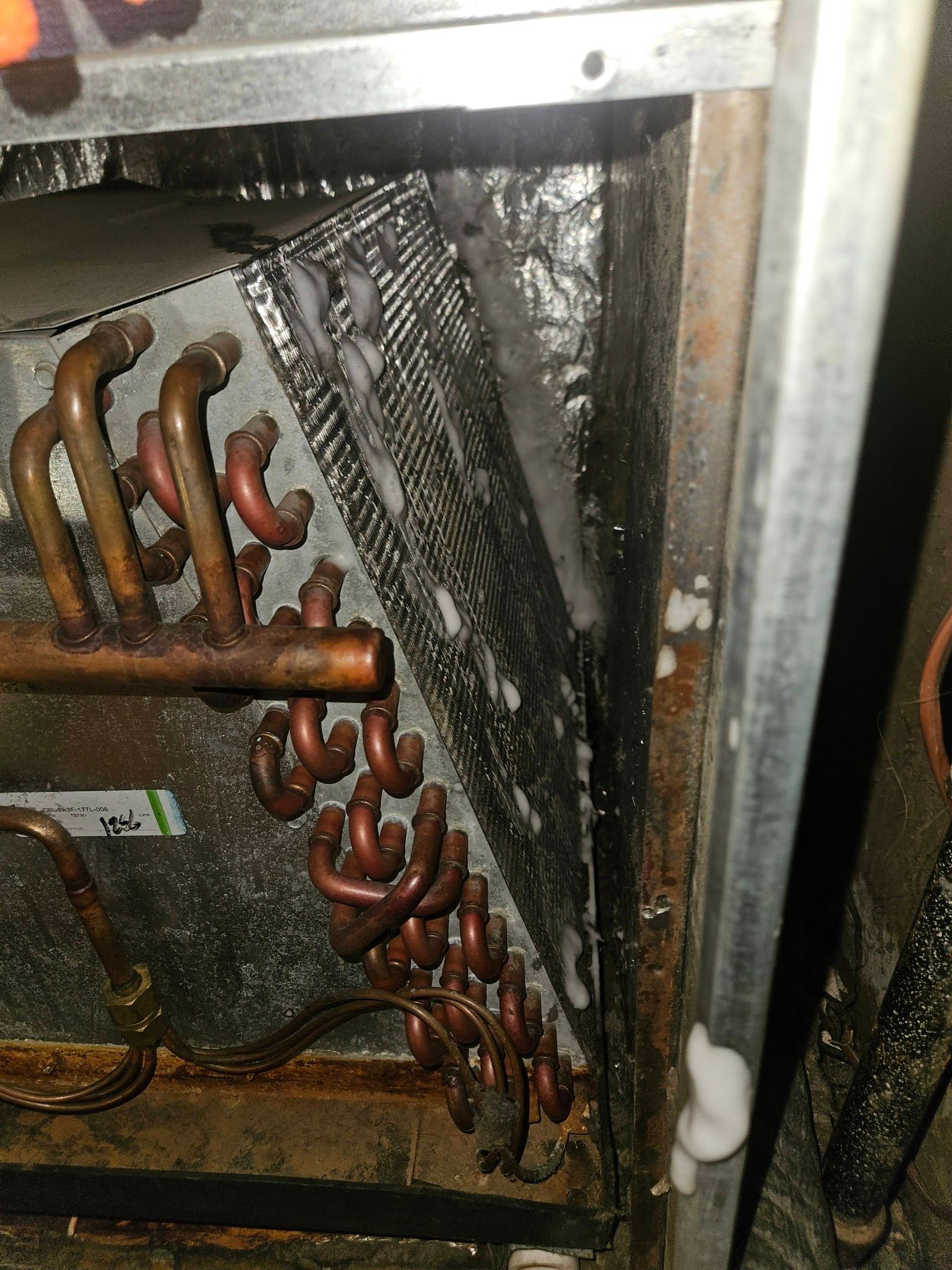 An indoor AC evaporator coil with significant frost buildup on the fins and surrounding metal cabinet.