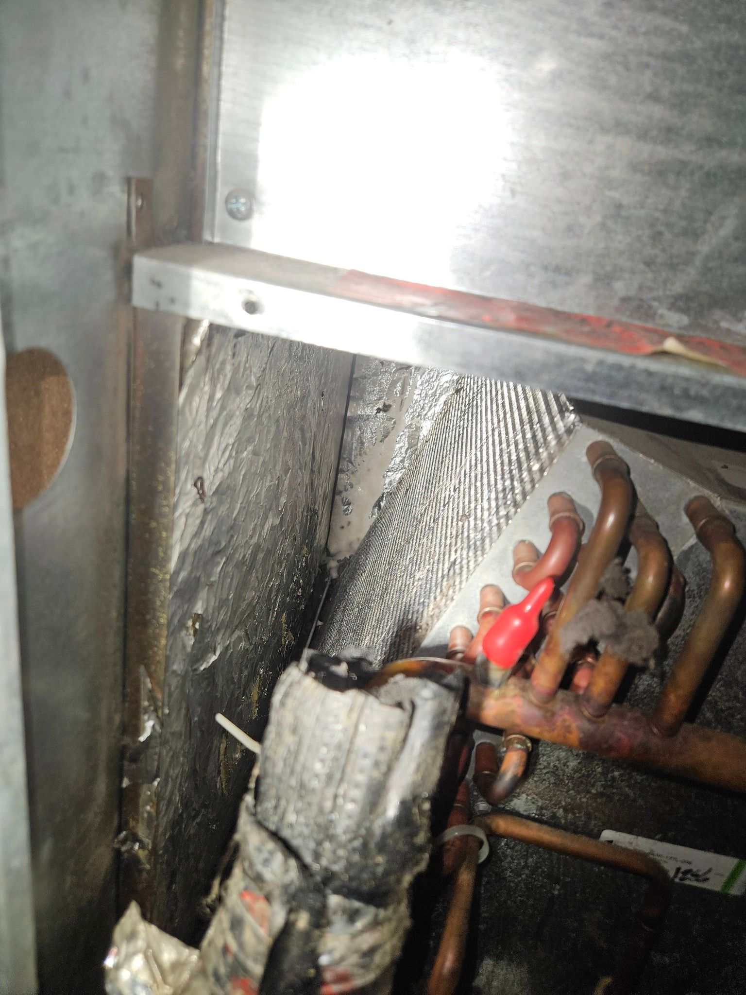 Internal view of an HVAC unit showing copper piping, insulation, and a red cap near a metal panel.