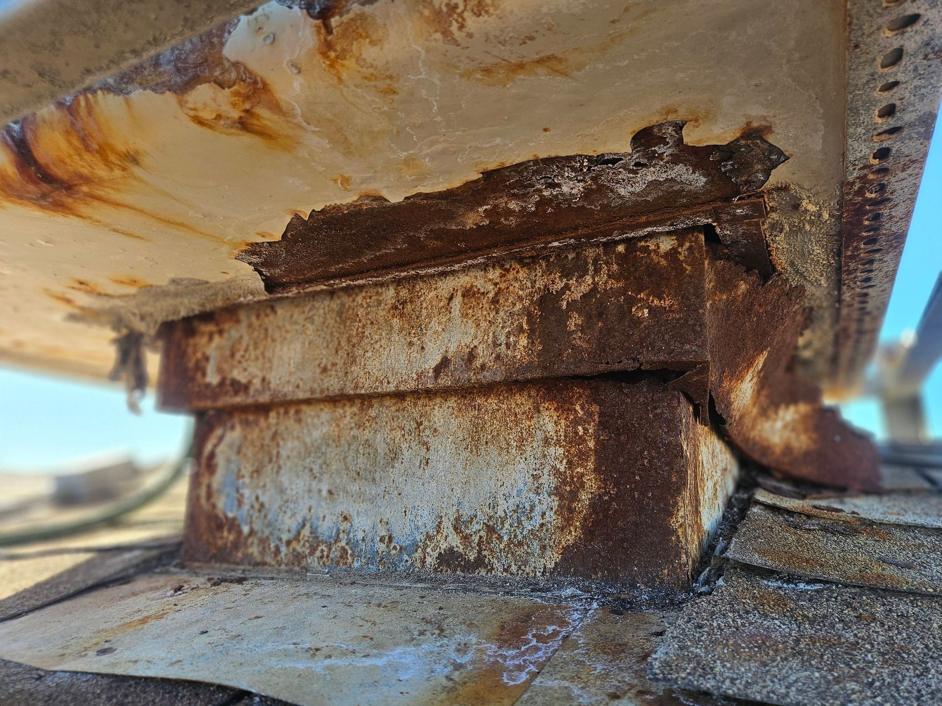 A severely rusted metal roof flashing vent on a shingled roof, showing significant corrosion and peeling paint.