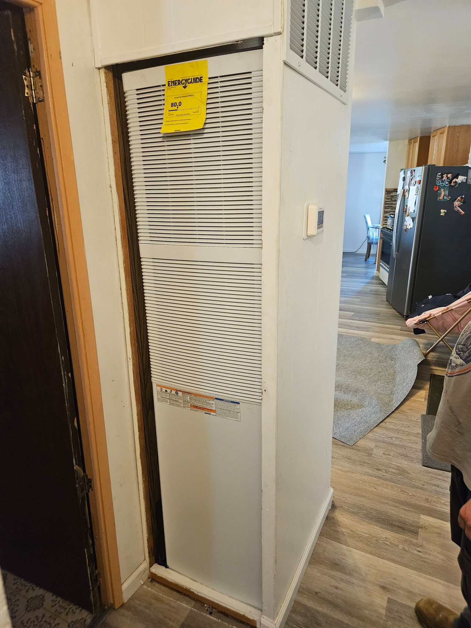 A tall, white indoor HVAC unit stands in a hallway corner with a yellow maintenance tag attached to the vented panel.