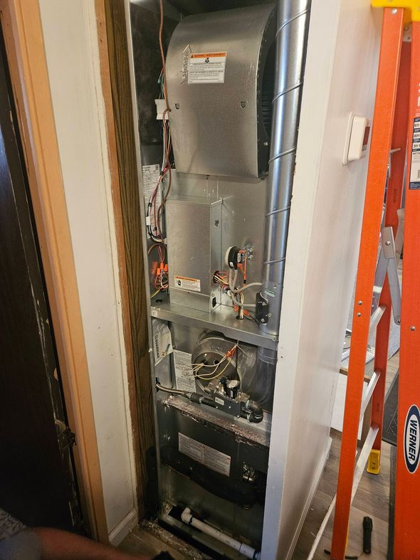 An open HVAC air handler unit in a narrow closet with an orange ladder standing to the right.
