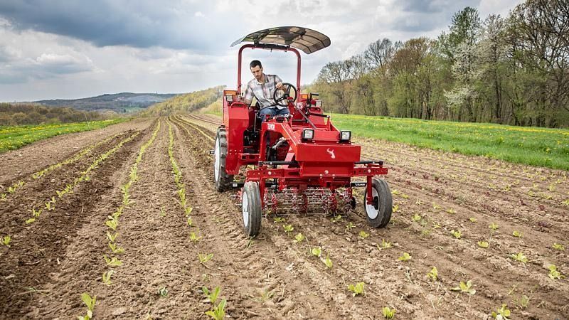 Red tractor cultivating rows in a field under a cloudy sky