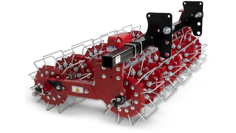 Red agricultural tiller with spiked wheels and black mounting brackets on a white background