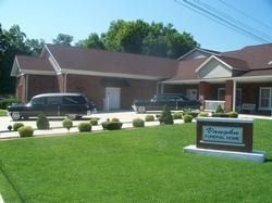 Single-story brick building with parked cars and a lawn sign on a sunny day