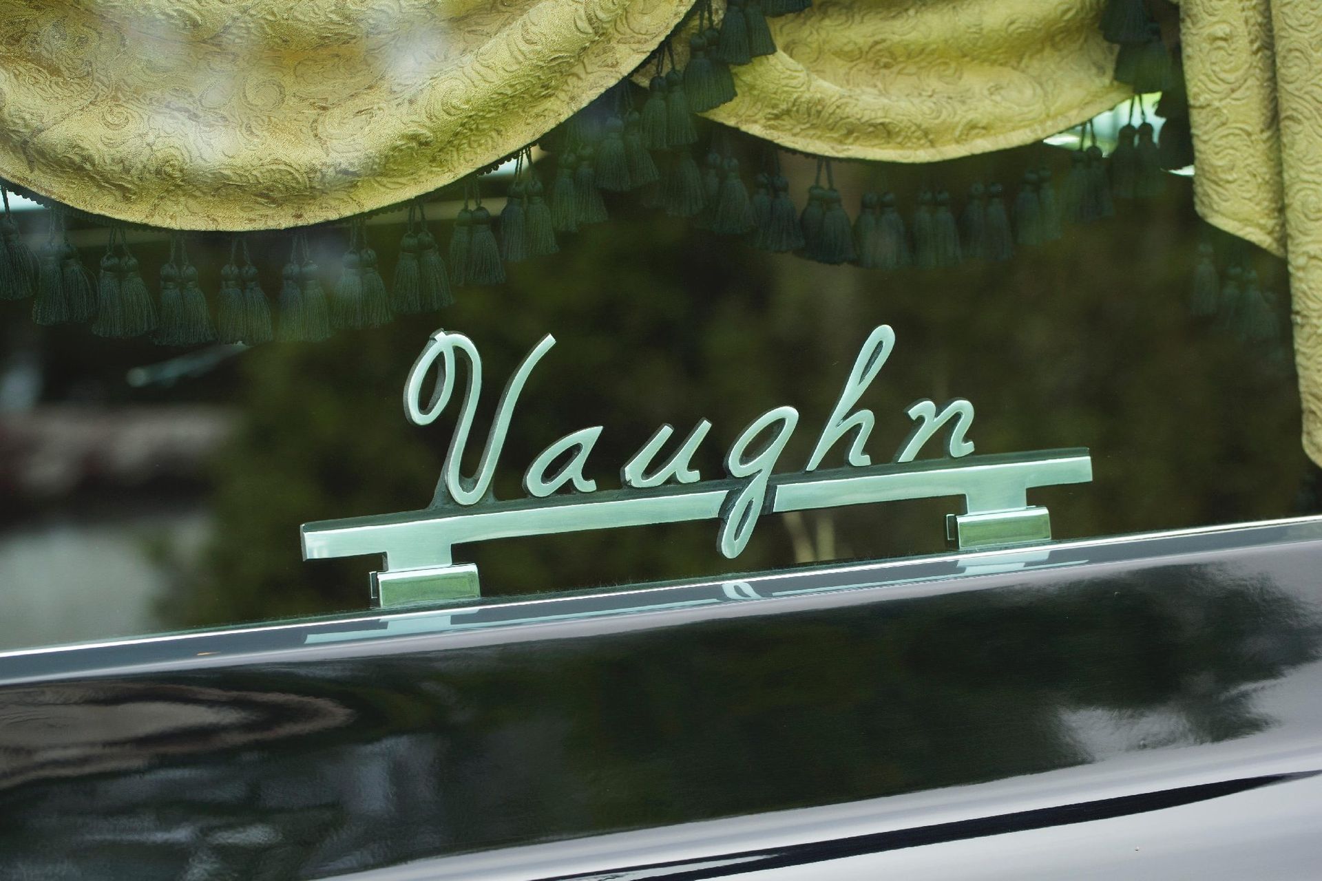 Name “Vaughn” in cursive on a car window with yellow curtains reflected above