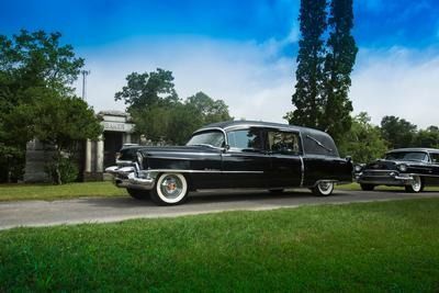 Classic black vintage sedan parked on a driveway beside a green lawn and trees under a blue sky