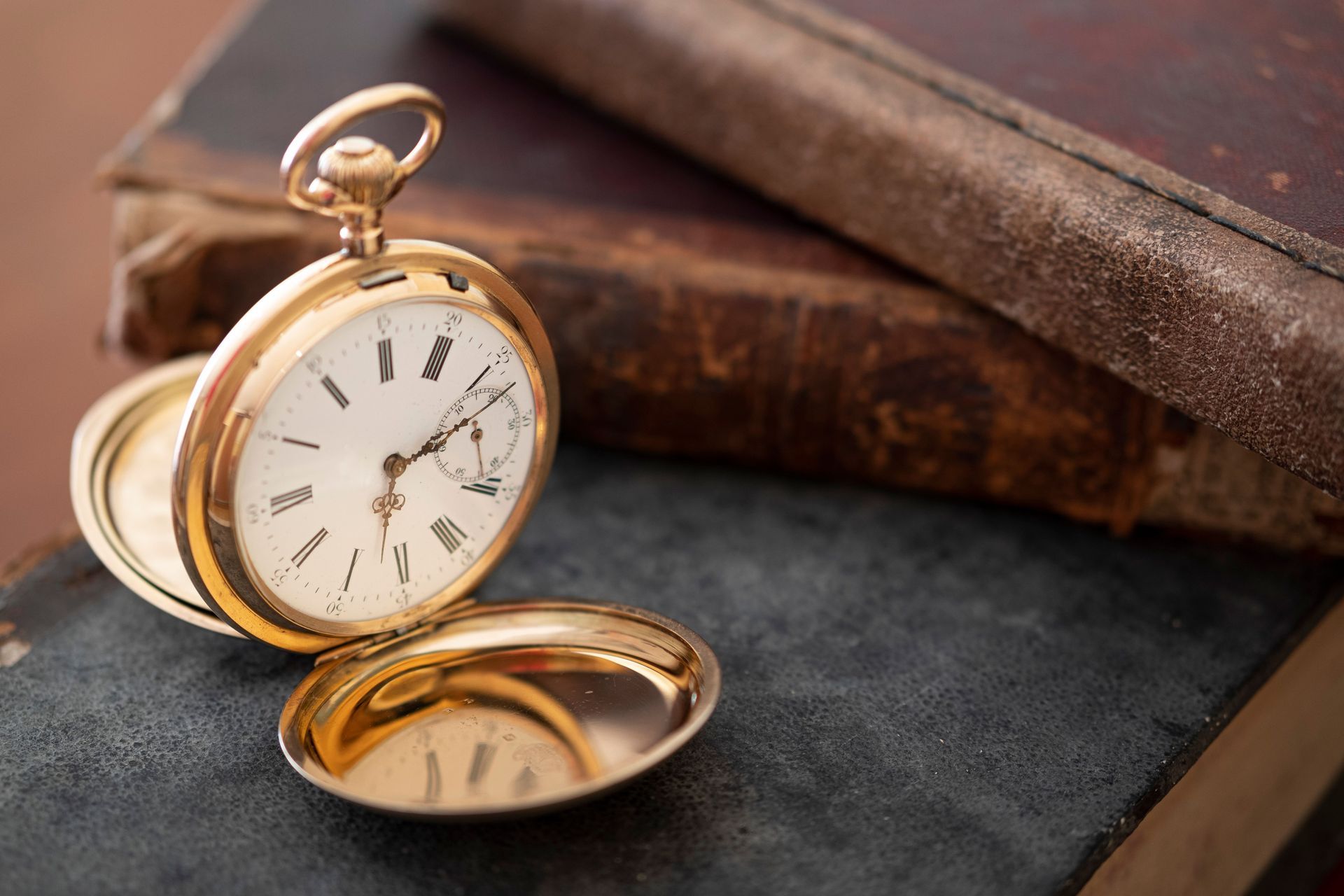 Gold pocket watch on a stack of old books, with its lid open beside it.