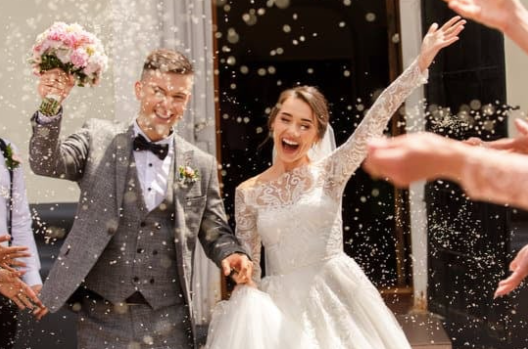 A bride and groom are being showered with rice by their wedding guests.