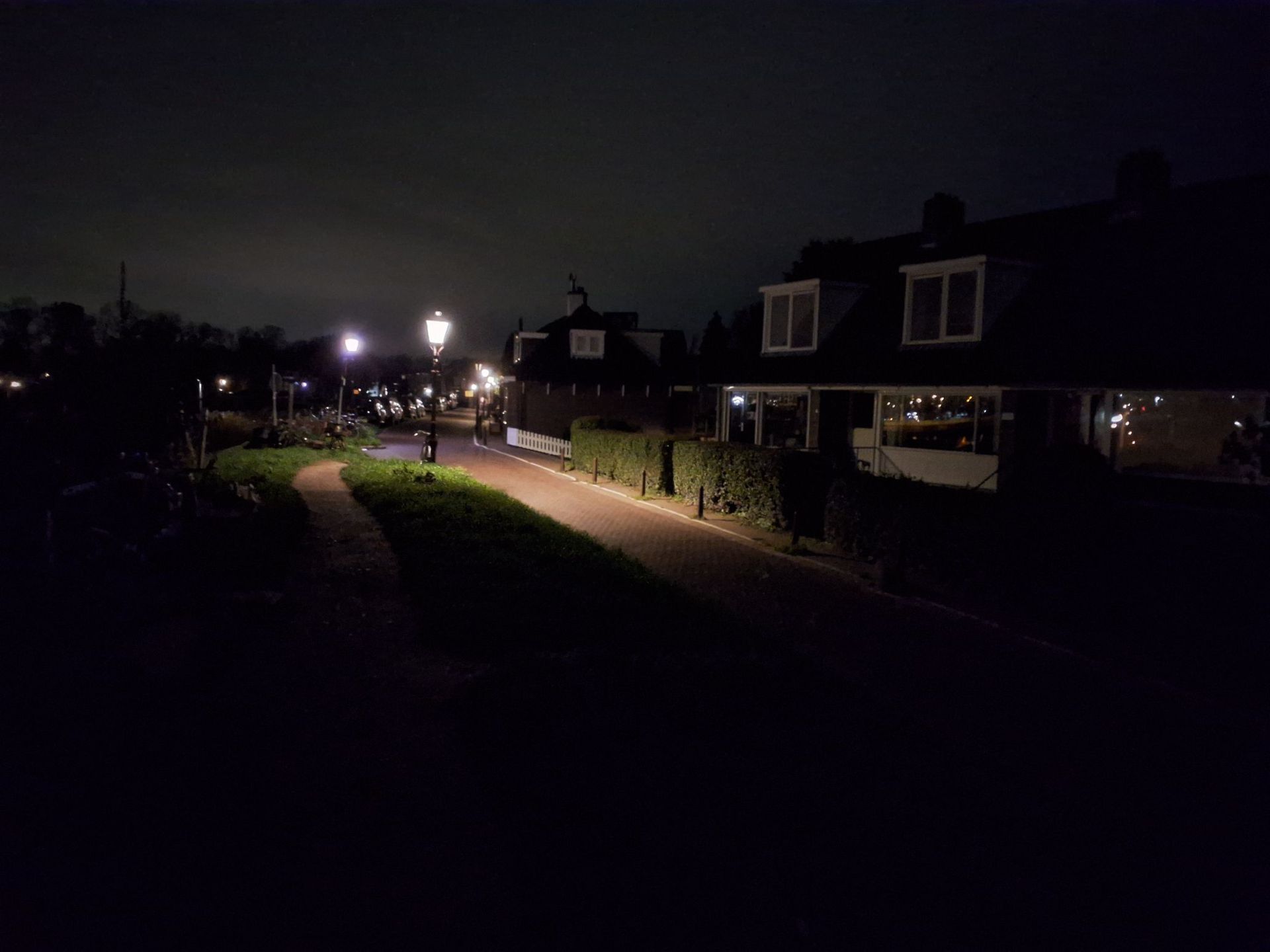 Een woonstraat 's nachts met verlichte lantaarnpalen, donkere huizen en een pad aan de linkerkant.