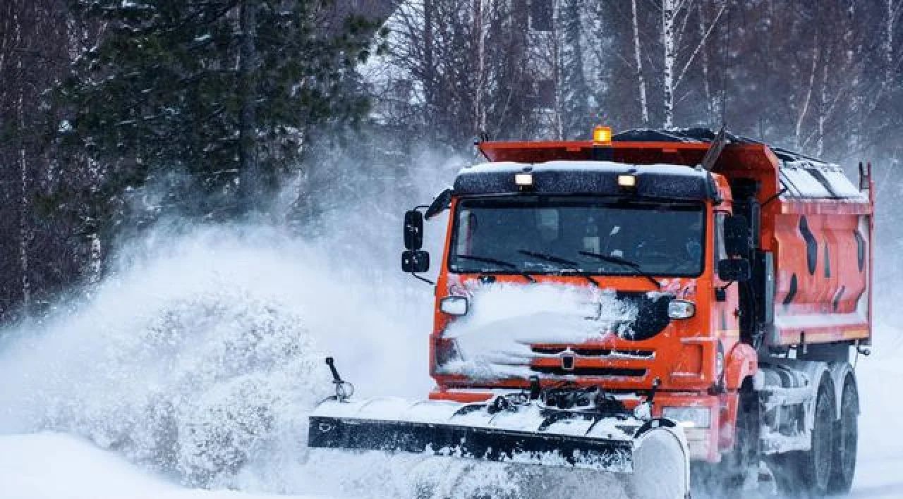 Orange snowplow clearing snow on a snowy road in a winter storm