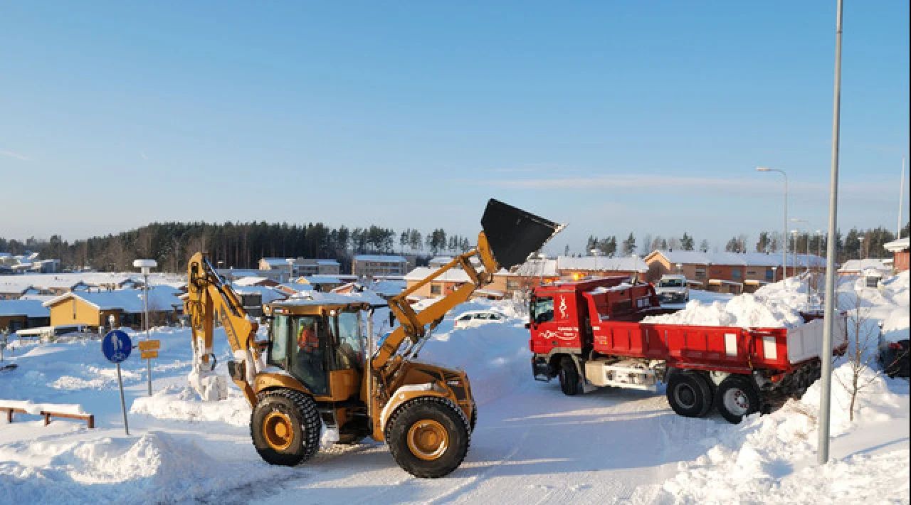 Yellow loader and red snow truck in a snowy lot under a clear blue sky