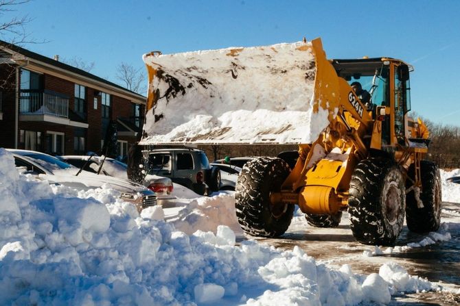 Yellow front loader clearing snow in a parking lot beside buildings