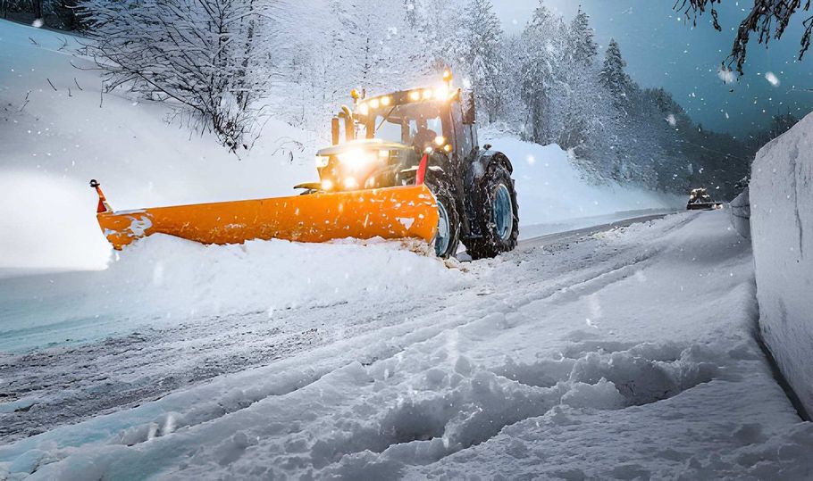 Orange snowplow clearing a snowy mountain road in heavy snowfall