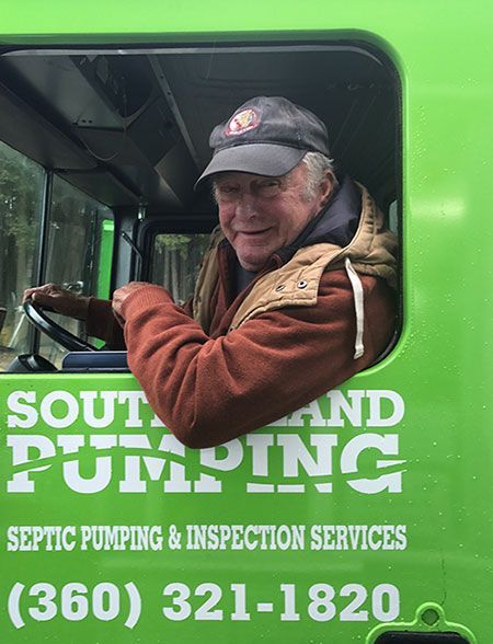 Man in green truck, smiling, holding steering wheel. 