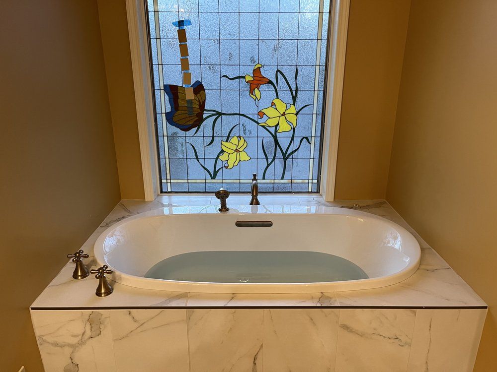 A bathtub in a bathroom with a stained glass window above it.