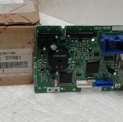 Primer plano de una placa de circuito verde junto a cajas de cartón, con conectores azules y chips negros.