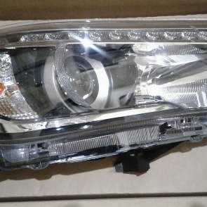 Primer plano de un faro de coche plateado con una lente reflectante brillante y una cubierta de plástico transparente.