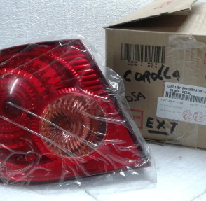 Conjunto de luces traseras rojas envuelto en plástico junto a una caja de cartón sobre una superficie blanca.