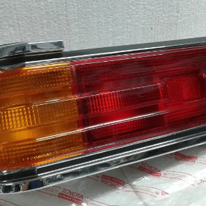 Primer plano de la luz trasera de un coche clásico con lentes rojas y ámbar y embellecedores cromados.