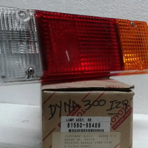 Luz trasera de vehículo roja, blanca y ámbar sobre una caja de repuestos Toyota con inscripciones manuscritas.