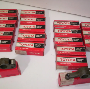 Pilas de cajas rojas y blancas de repuestos originales Toyota con pequeños componentes metálicos sobre una superficie blanca.