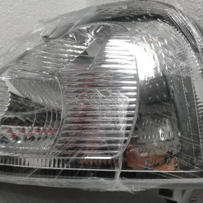 Primer plano de un faro de coche transparente con reflector cromado y lente texturizada.