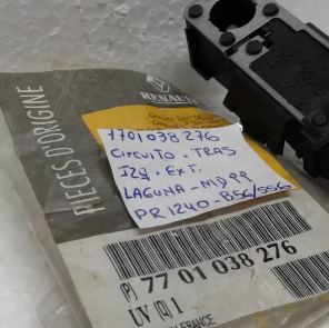 Primer plano de un paquete de piezas Renault con etiqueta manuscrita, código de barras y un componente de plástico negro en la parte superior.