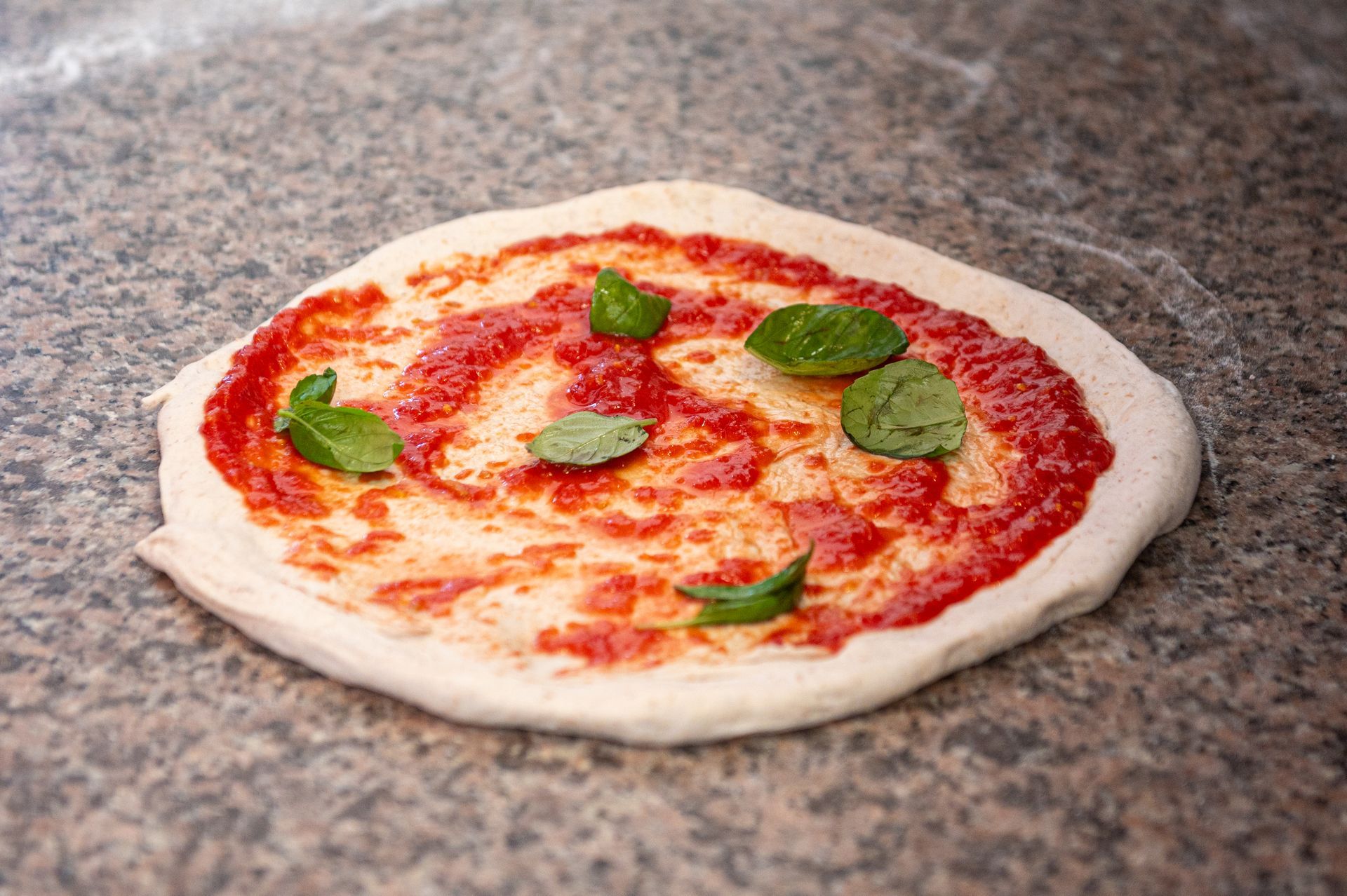 Una pizza con salsa di pomodoro e basilico è appoggiata su un tavolo.