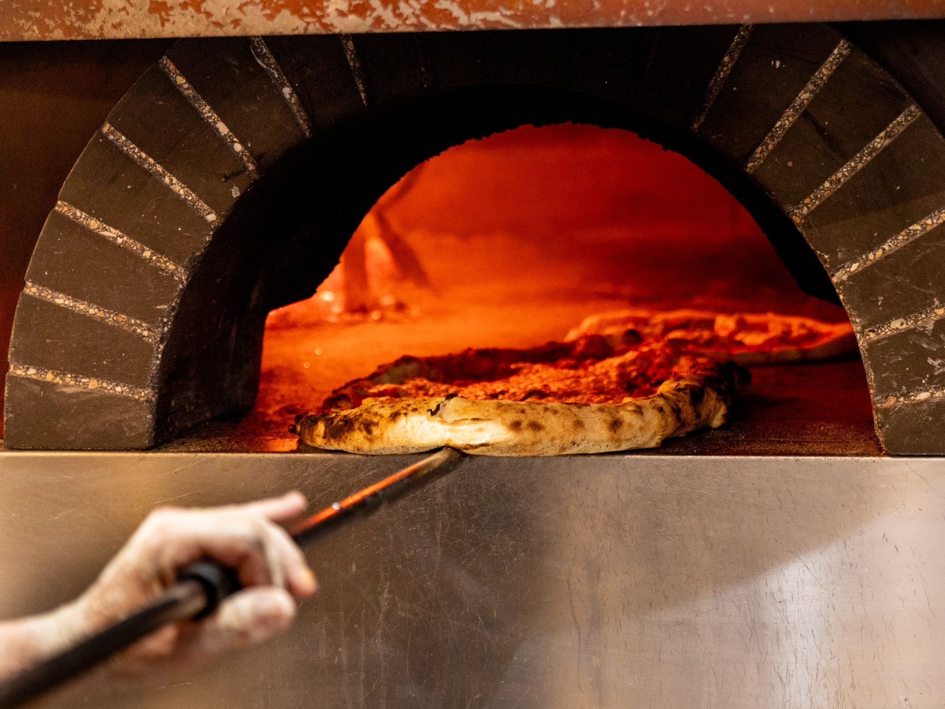 Una persona sta spalmando la salsa di pomodoro sull'impasto della pizza.
